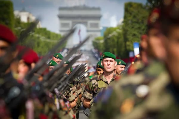Des soldats en défilé, bérets verts, sur une grande avenue.